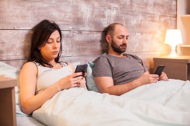 Pareja caucásica aburrida antes de irse a dormir navegando en el teléfono inteligente.