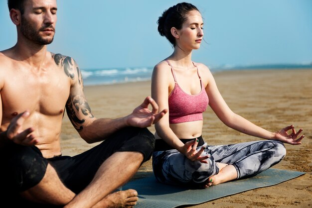 La pareja caucásica medita en la playa