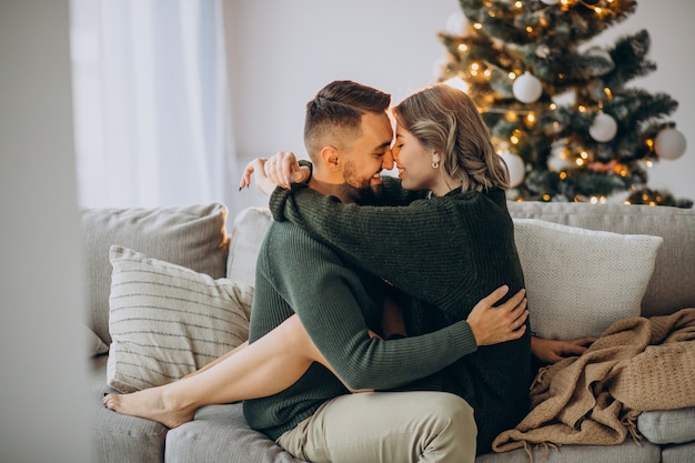 Pareja celebrando la Navidad juntos en casa, besándose junto al árbol de Navidad