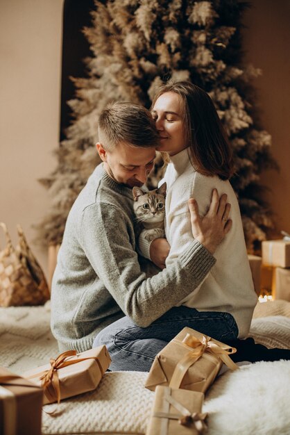 Pareja celebrando la Navidad con su gato junto al árbol de Navidad