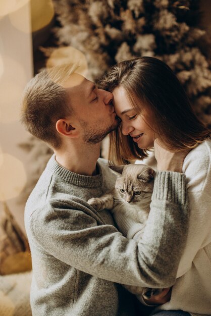 Pareja celebrando la Navidad con su gato junto al árbol de Navidad