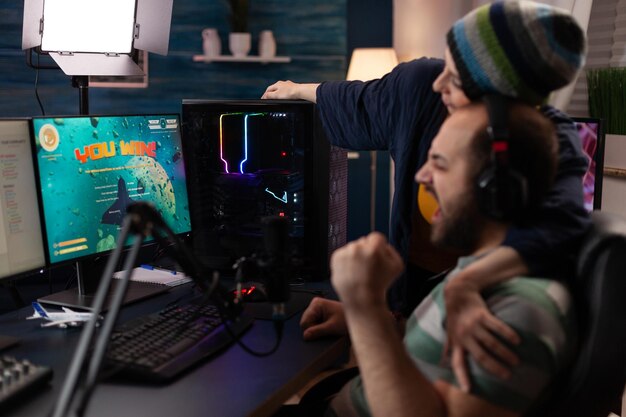 Pareja celebrando videojuegos gana en transmisión en vivo. La mujer se siente feliz porque el hombre gana el juego mientras está transmitiendo en línea con el chat en la computadora. Streamer con equipo de juego