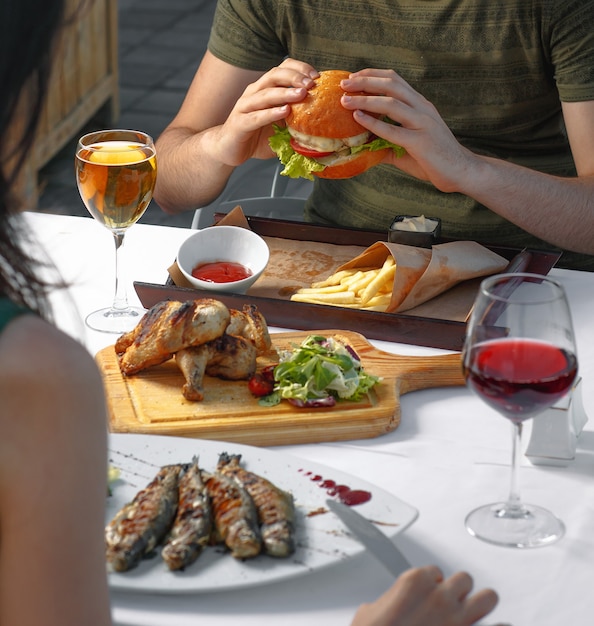 Pareja cenando con hamburguesa, pescado y blanco, vino tinto.