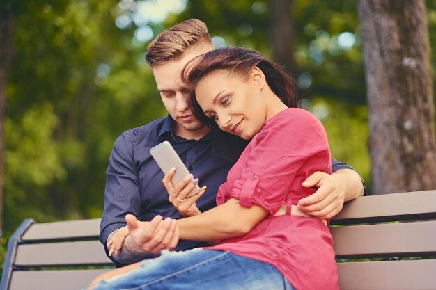 Una pareja en una cita en un parque de la ciudad usando un teléfono inteligente y mensajería instantánea.