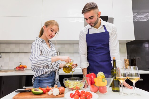 Pareja cocinando ensalada de verduras con aceite de oliva.