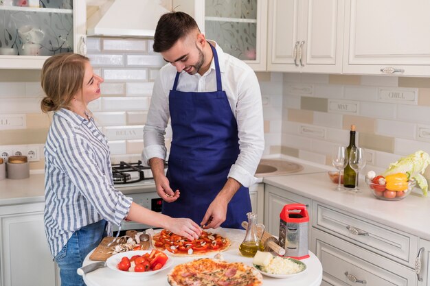 Pareja cocinando pizza con champiñones y verduras