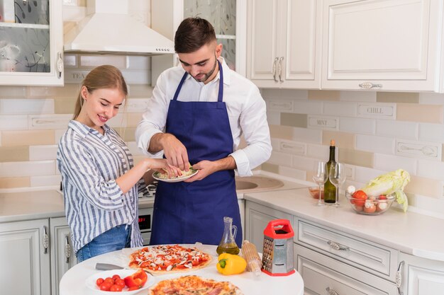 Pareja cocinando pizza con queso en la cocina