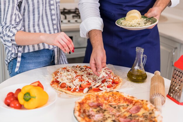 Pareja cocinando pizza con queso en la mesa