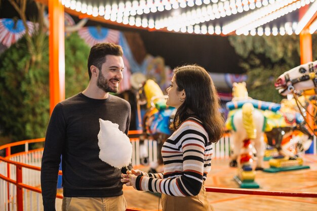 Pareja comiendo algodón de azúcar en el parque de atracciones