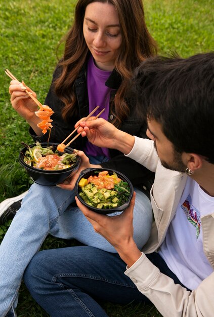 Pareja comiendo tazón de salmón en el césped al aire libre