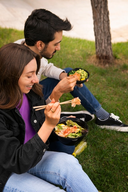 Pareja comiendo tazón de salmón en el césped al aire libre