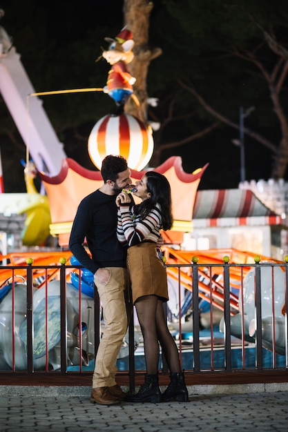 Foto gratuita pareja comiéndose una piruleta en el parque de atracciones