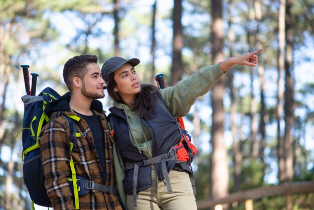 Pareja concentrada de jóvenes excursionistas. Hombre caucásico con barba y mujer con gorra con grandes mochilas señalando, discutiendo la ruta. Hobby, naturaleza, concepto de amor.