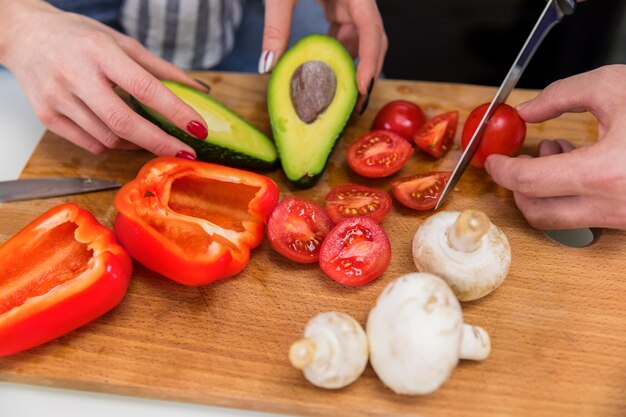 Pareja cortar diferentes verduras en tablero de madera