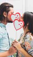 Foto gratuita pareja cubriendo caras con corazones de papel en palo