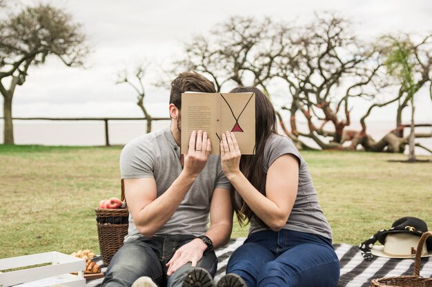 Pareja cubriéndose la cara con un libro en un picnic en el parque