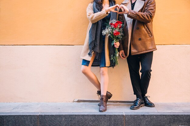 Pareja de cultivos con ramo que muestra gesto de corazón