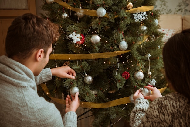 Pareja decorando arbol de navidad con bolas de plata.