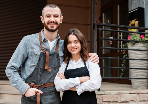 Pareja en delantales posando fuera de cafetería