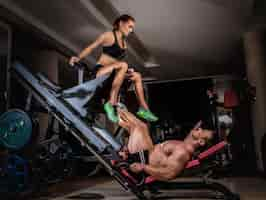 Foto gratuita la pareja deportiva está haciendo ejercicio en el gimnasio. hombre levantador de pesas haciendo prensas de piernas con su entrenador.