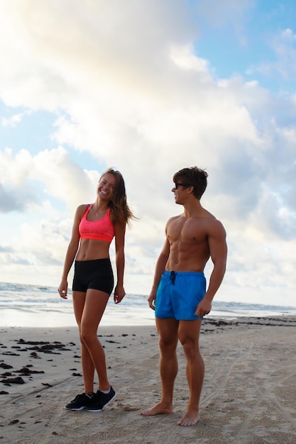 Foto gratuita pareja deportiva de hombre y mujer sin camisa posando en una playa.