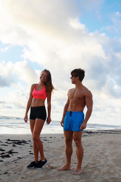 Pareja deportiva de hombre y mujer sin camisa posando en una playa.