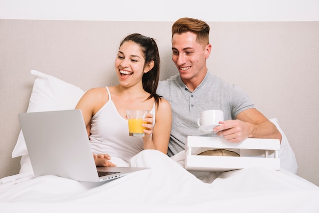 Pareja desayunando y riendo mirando portátil