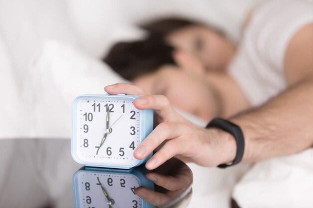 Pareja despertada por alarma, hombre apagando el timbre del reloj