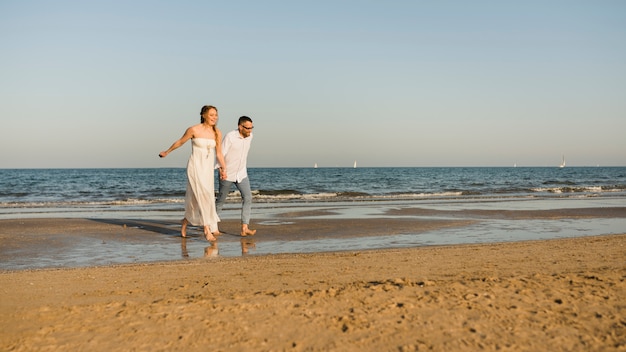 Pareja despreocupada cogidos de la mano del otro corriendo a la orilla del mar