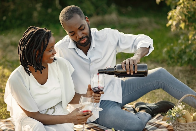 Pareja despreocupada y relajada disfrutando juntos del picnic. Hombre estudiando detenidamente el vino en un vaso.