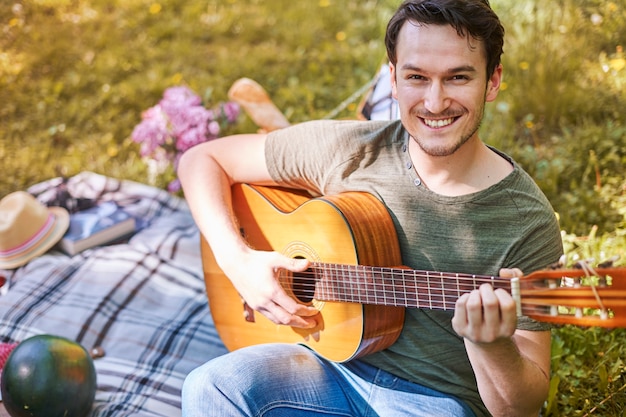 Pareja disfrutando de un picnic en el parque. Hombre tocando la guitarra. Cita romántica