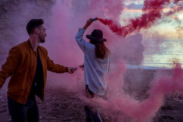 Pareja divirtiéndose con bomba de humo rosa en la orilla del mar