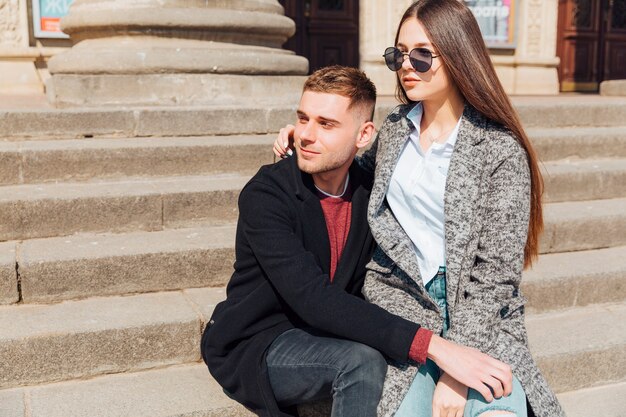 Pareja elegante sentada en las escaleras y mirando en una dirección