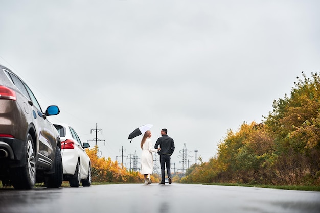 Pareja enamorada en la carretera fuera de la ciudad bajo un cielo gris cerca de los autos