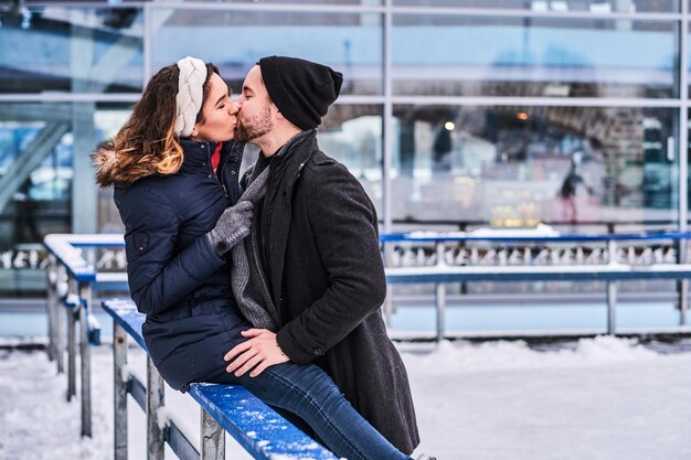 Pareja enamorada, cita en la pista de hielo, una chica sentada en una barandilla y abrazando a su novio.