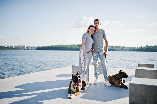 Pareja enamorada de dos perros pit bull terrier contra el lado de la playa