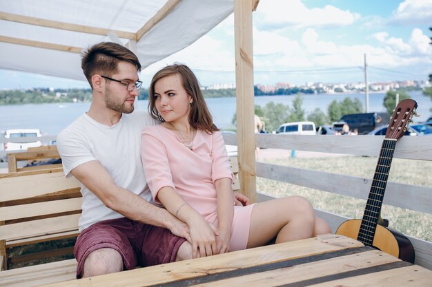 Pareja enamorada sentada en un banco de madera con una guitarra al lado