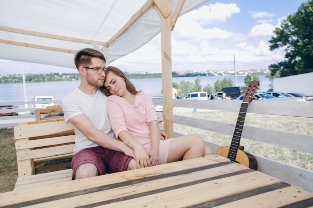 Pareja enamorada sentada en un banco de madera con una guitarra al lado