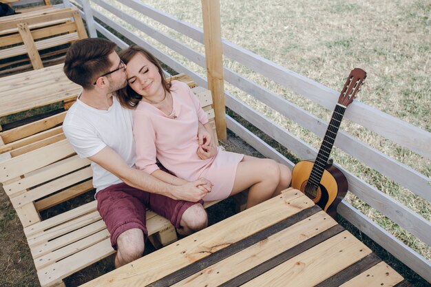 Pareja enamorada sentada en un banco de madera con una guitarra al lado