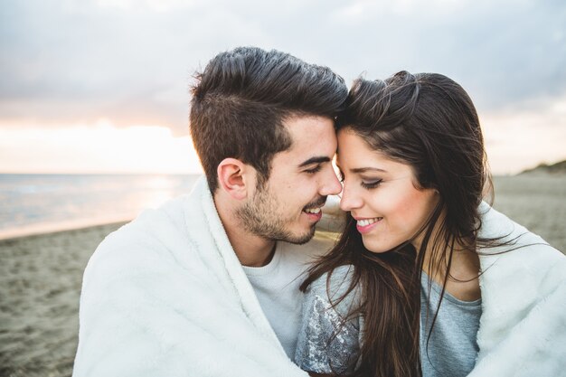 Pareja enamorada sentada en una playa cubierta por una manta blanca