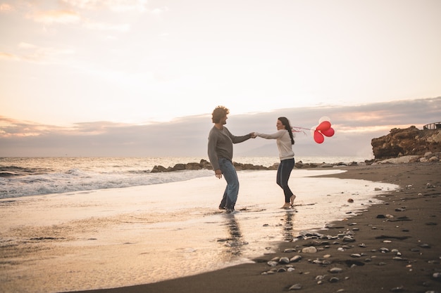 Pareja enamorada tirándose de las manos y ella con globos en la mano