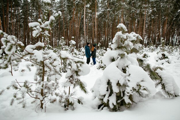 Pareja de enamorados caminando en el bosque de pinos cubiertos de nieve. Historia de amor de invierno.
