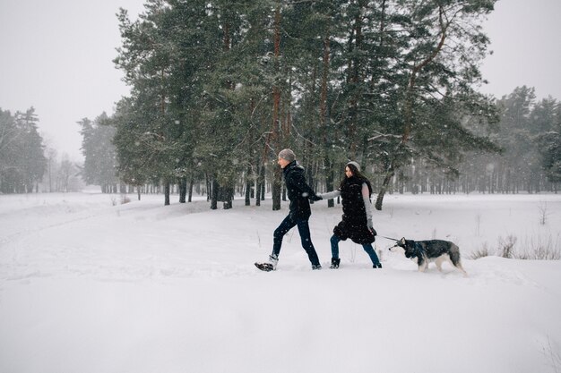 Pareja de enamorados caminando con su perro Husky en el clima de invierno cubierto de nieve