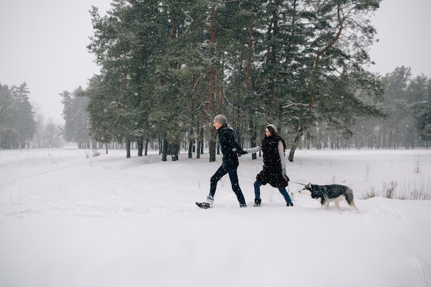 Pareja de enamorados caminando con su perro Husky en el clima de invierno cubierto de nieve