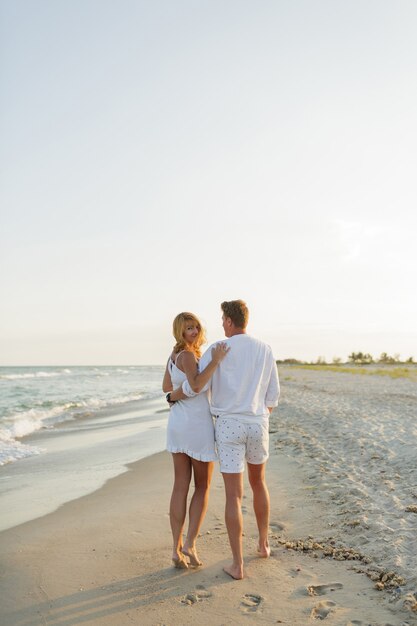 Pareja de enamorados en ropa blanca caminando por la playa. De longitud completa.