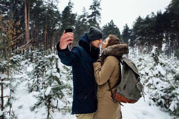 Pareja de enamorados toma selfie en teléfono móvil en el bosque de invierno cubierto de nieve