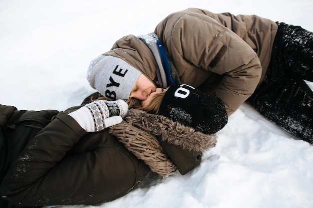 Una pareja de enamorados tumbados en la nieve y besándose. Historia de amor de invierno.