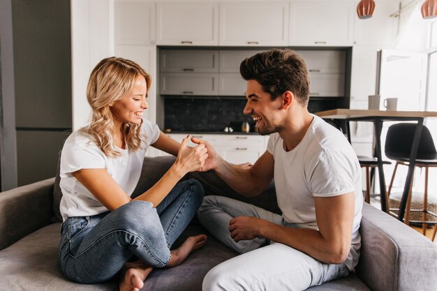 Pareja energizada jugando con los pulgares en el sofá Chica graciosa riéndose tratando de vencer a su novio se ve muy alegre