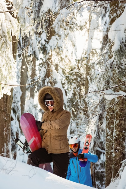 Pareja con esquí y snowboard caminando en la montaña nevada