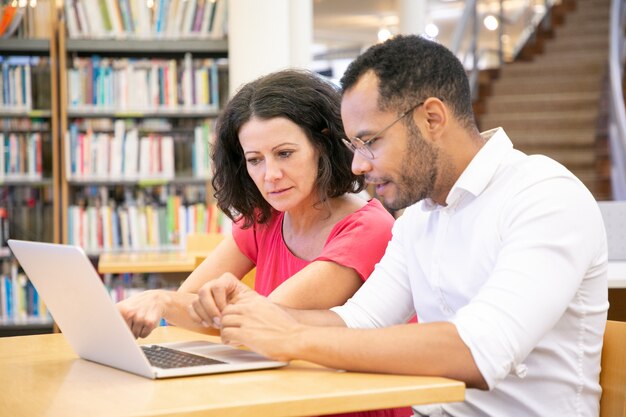 Pareja de estudiantes universitarios adultos que miran contenido en la computadora